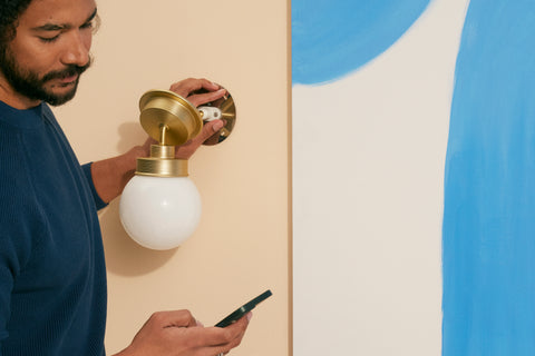 man changing light fixture while looking at phone